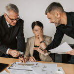 Three people reviewing a work assignment with two men making comments and the woman looking overwhelmed.